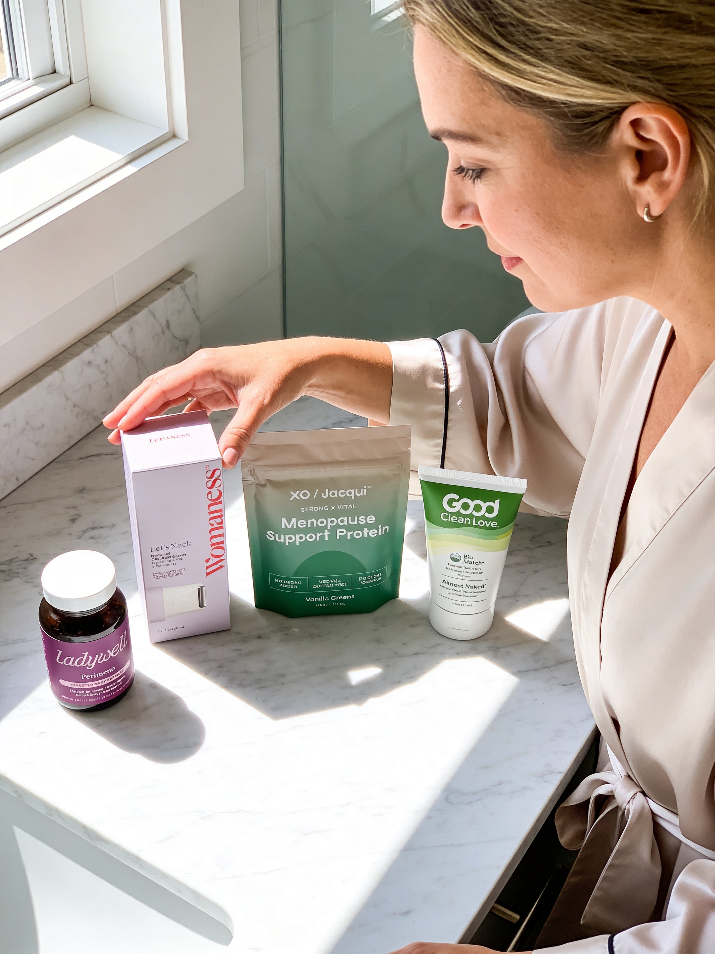 Woman in a robe looking at menopause support products on a table by a window