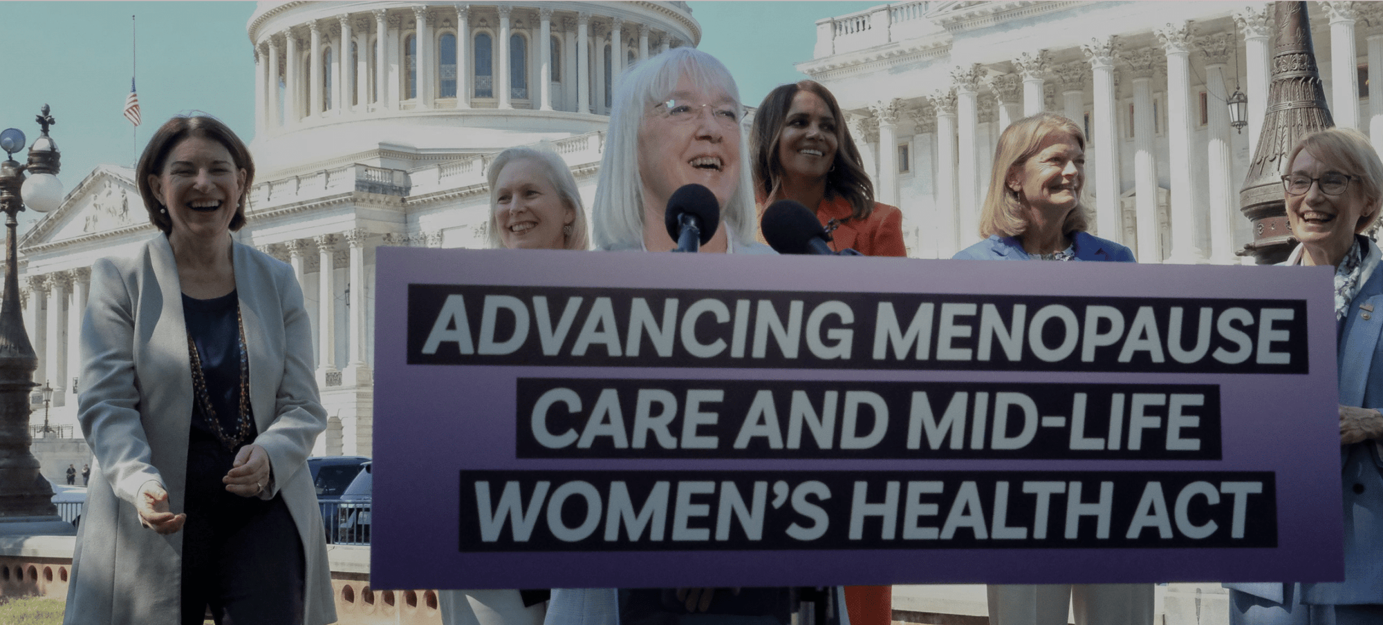 Group of women holding a sign in front of a building, advocating for menopause care and mid-life women's health act.